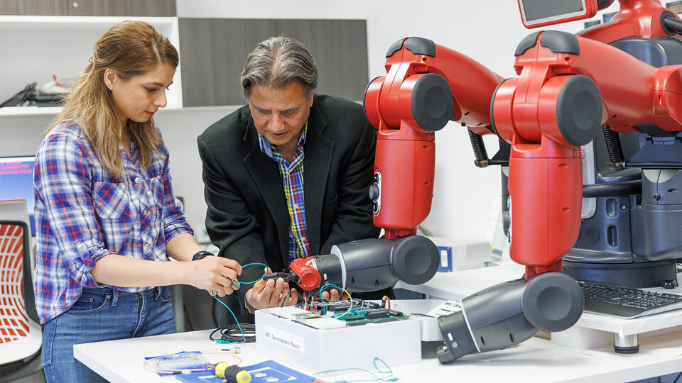 Student and faculty adjusting electrical wiring on robot